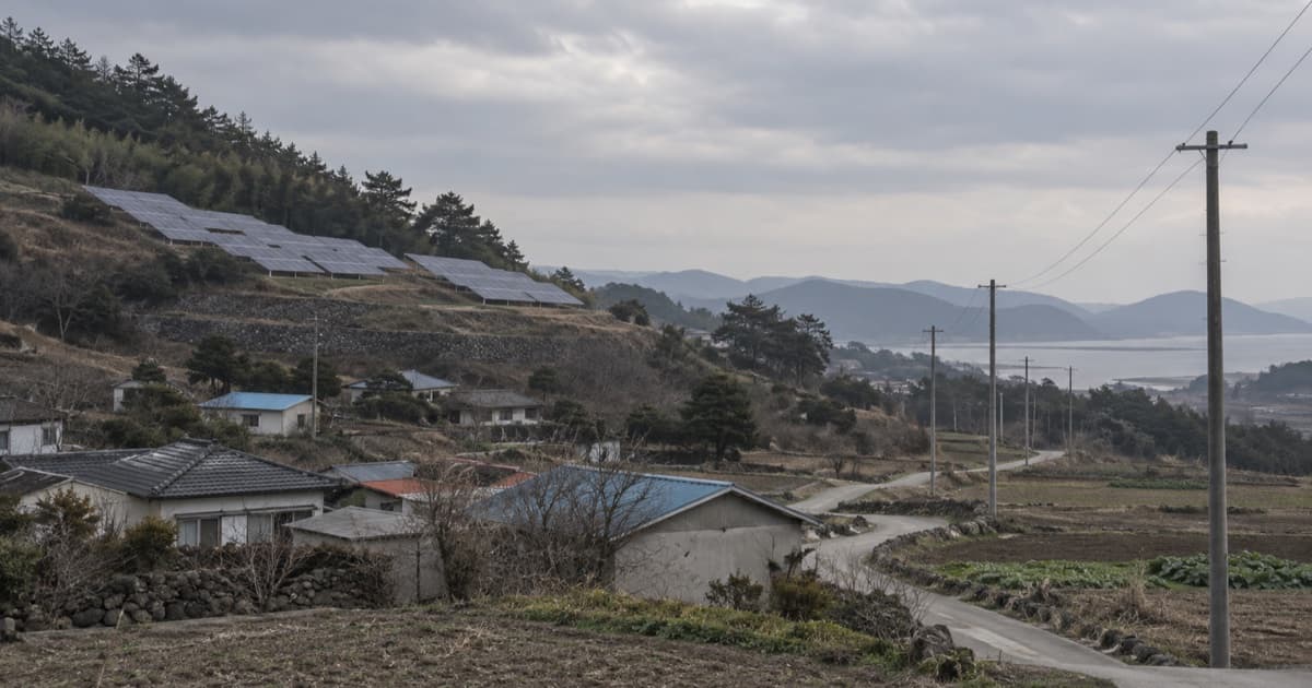 농촌 마을 뒤편 언덕의 태양광 패널과 도로를 따라 선 전봇대가 흐린 하늘 아래 놓인 AI 생성 일러스트